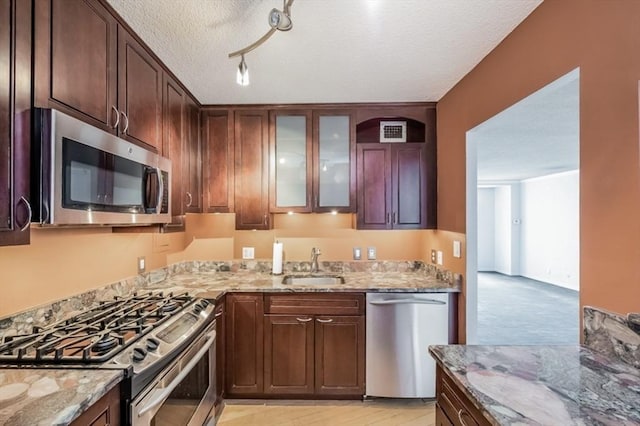 99 Pond Ave Unit 608, Brookline, MA 02445 - kitchen featuring stainless steel appliances, a sink, light stone counters, a textured ceiling, and glass insert cabinets