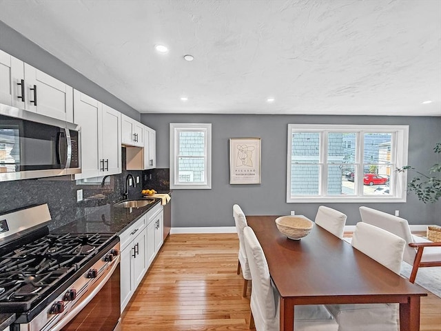 kitchen featuring appliances with stainless steel finishes, a sink, light wood-type flooring, baseboards, and decorative backsplash