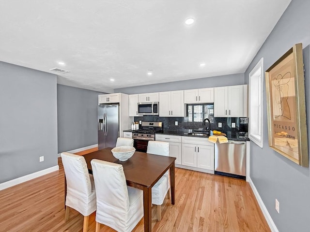 kitchen with appliances with stainless steel finishes, a sink, white cabinetry, tasteful backsplash, and light wood-type flooring