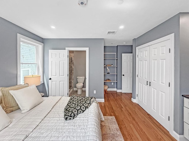 bedroom featuring wood finished floors, a closet, baseboards, ensuite bath, and recessed lighting