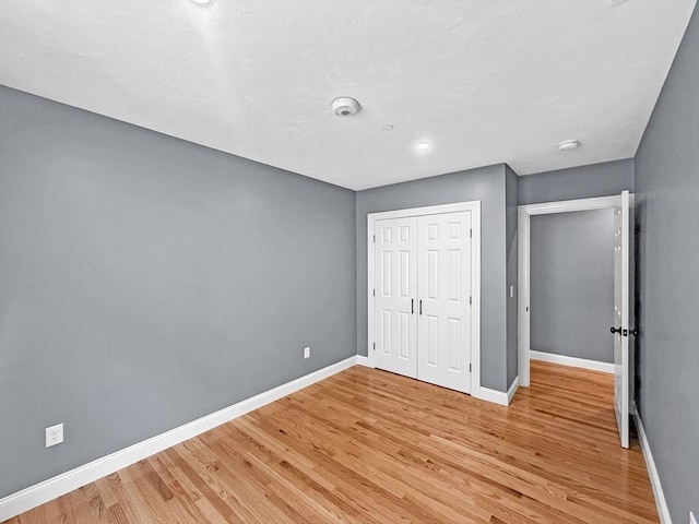 unfurnished bedroom with baseboards, light wood-style floors, and a closet