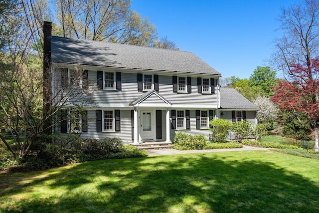 colonial-style house featuring a chimney and a front lawn