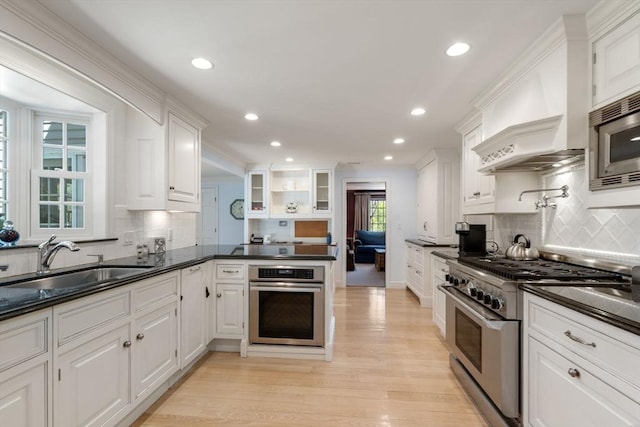 kitchen featuring backsplash, a sink, white cabinets, stainless steel appliances, and light wood-style flooring