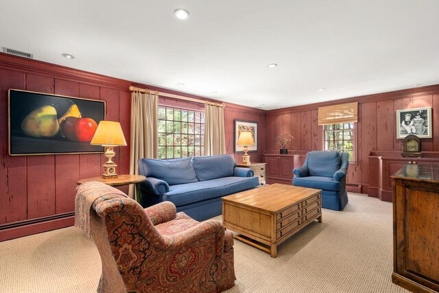 living room with light carpet, baseboard heating, wood walls, a baseboard radiator, and visible vents