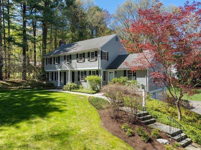 colonial home featuring a shingled roof, a chimney, and a front yard