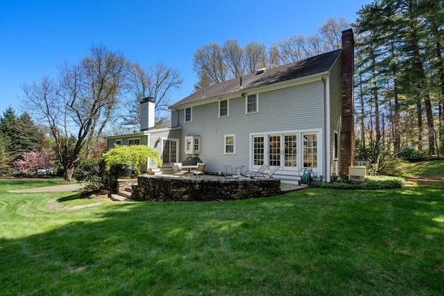 back of house featuring a lawn, a chimney, and a patio area