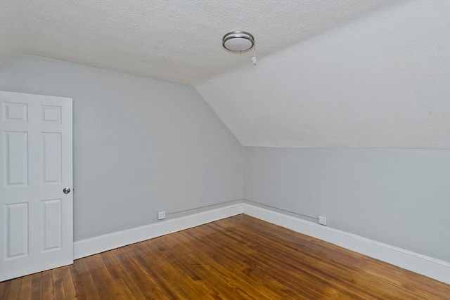 additional living space with wood-type flooring, vaulted ceiling, and a textured ceiling