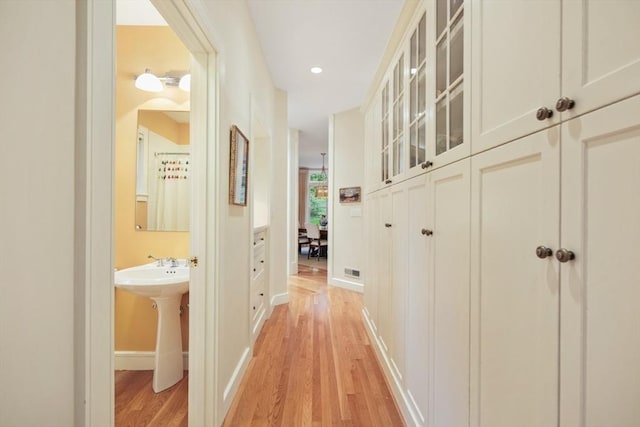 hall with light wood finished floors, baseboards, visible vents, a sink, and recessed lighting