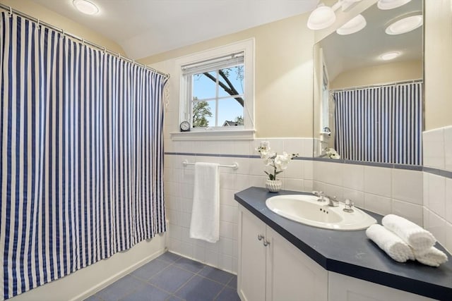 full bathroom featuring shower / tub combo, wainscoting, tile patterned flooring, vanity, and tile walls