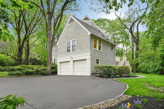 view of side of home featuring a garage, driveway, a shingled roof, stairway, and a yard