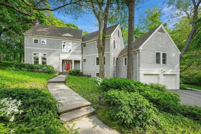 view of front facade featuring driveway, a chimney, and an attached garage