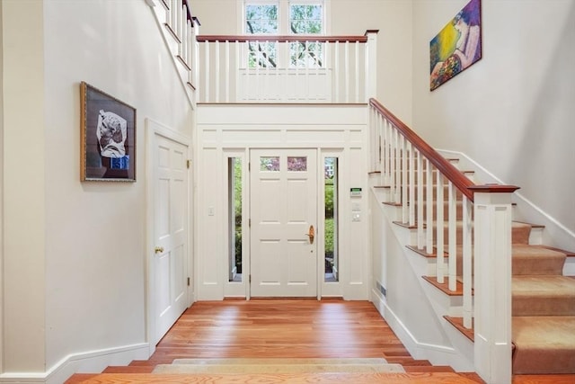 foyer featuring light wood finished floors, a high ceiling, stairs, and baseboards