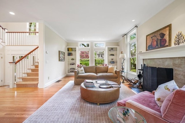 living room featuring stairway, a fireplace with flush hearth, light wood-style flooring, and crown molding