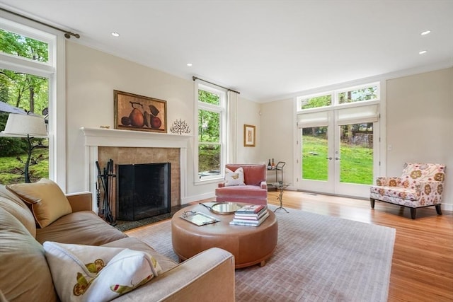 living area featuring french doors, light wood finished floors, recessed lighting, ornamental molding, and a tile fireplace