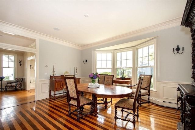 dining space featuring wood-type flooring, a healthy amount of sunlight, crown molding, and a baseboard radiator