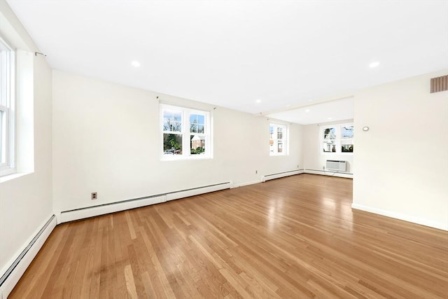 spare room with light wood-type flooring, an AC wall unit, and baseboard heating