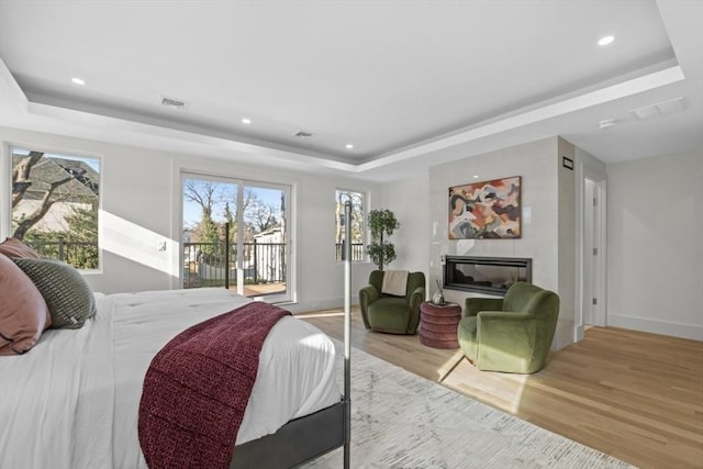 bedroom featuring a raised ceiling, access to outside, and light hardwood / wood-style floors