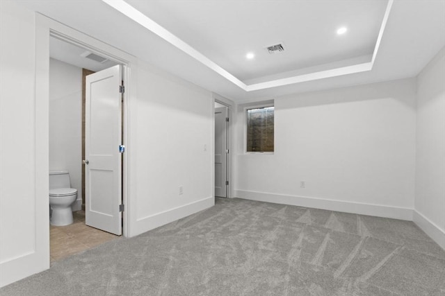 unfurnished bedroom featuring ensuite bath, a raised ceiling, and light carpet