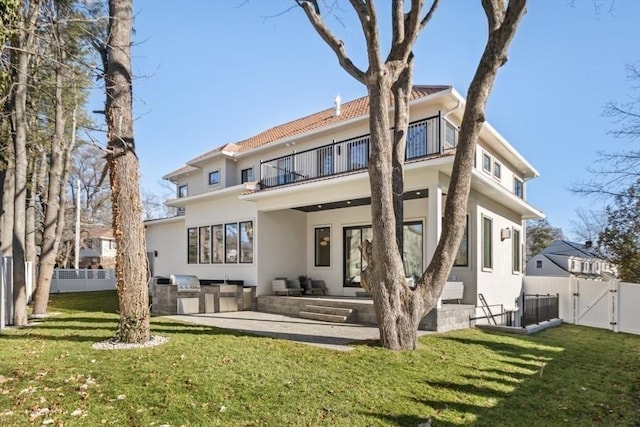 back of house with exterior kitchen, a balcony, a lawn, and a patio area