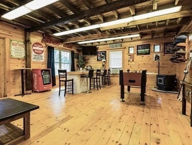 rec room featuring wood walls, hardwood / wood-style floors, a wood stove, and beamed ceiling