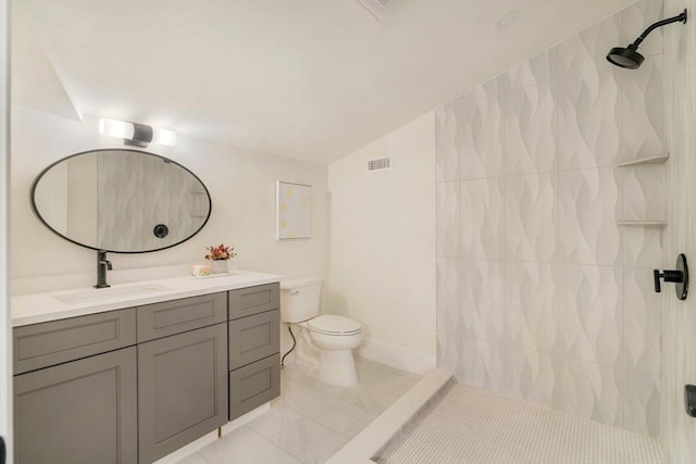 bathroom featuring toilet, vanity, a tile shower, and lofted ceiling