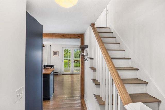 stairway with wood finished floors, french doors, a baseboard heating unit, beam ceiling, and baseboards