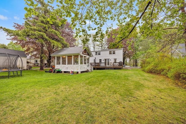 back of house featuring a trampoline, a sunroom, a wooden deck, and a yard