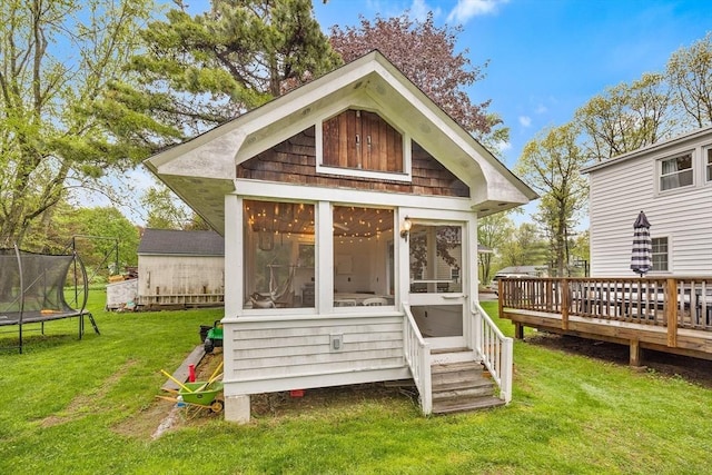 back of house featuring a trampoline, a wooden deck, a yard, and a sunroom