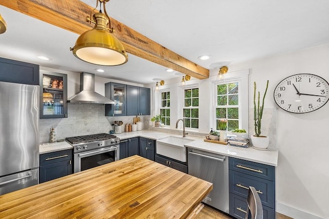 kitchen featuring stainless steel appliances, wall chimney exhaust hood, a sink, decorative backsplash, and glass insert cabinets