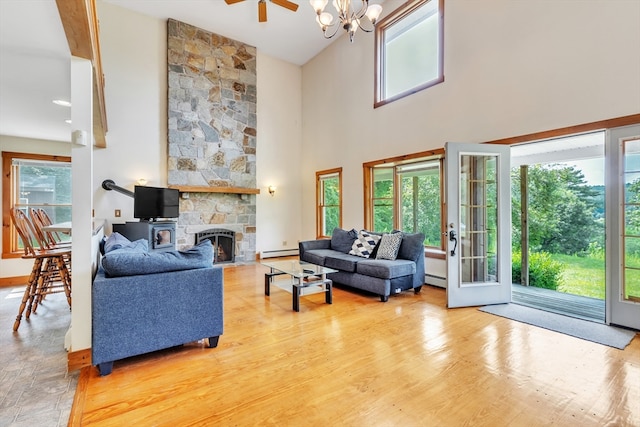 living room with light hardwood / wood-style floors, a high ceiling, a fireplace, ceiling fan with notable chandelier, and baseboard heating