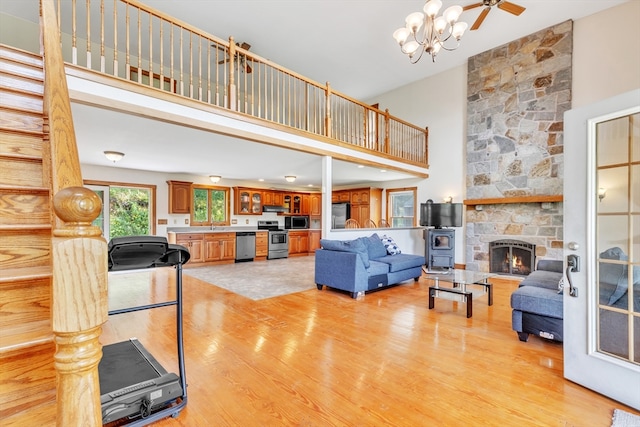 living room with ceiling fan with notable chandelier, a high ceiling, light hardwood / wood-style flooring, and a fireplace