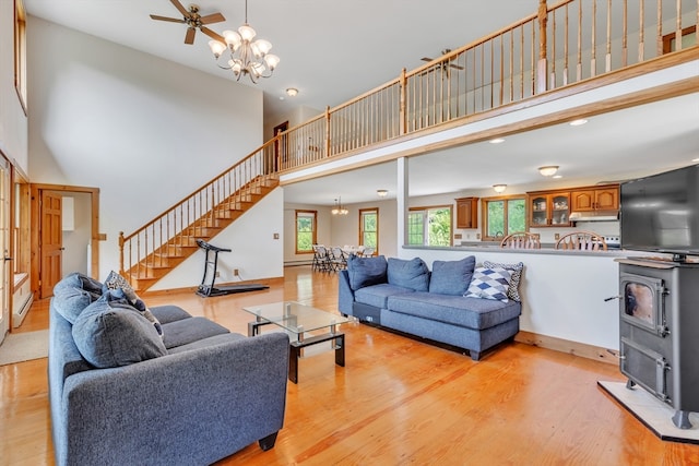 living room featuring ceiling fan with notable chandelier, a high ceiling, light hardwood / wood-style flooring, and a wood stove