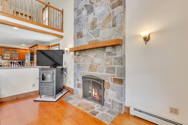 living room with a baseboard radiator, light hardwood / wood-style flooring, a wood stove, and a fireplace