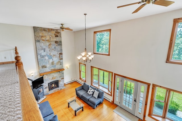 living room with light wood-type flooring, ceiling fan with notable chandelier, a baseboard radiator, and a stone fireplace