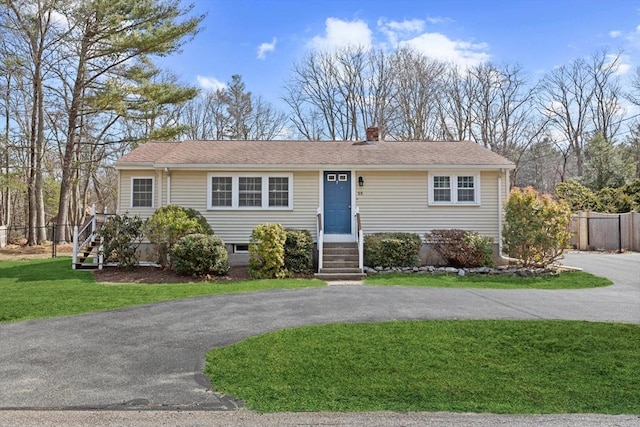 view of front facade with driveway, a chimney, a front lawn, and fence