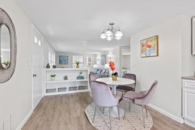 dining space featuring baseboards, visible vents, light wood-style flooring, decorative columns, and a chandelier