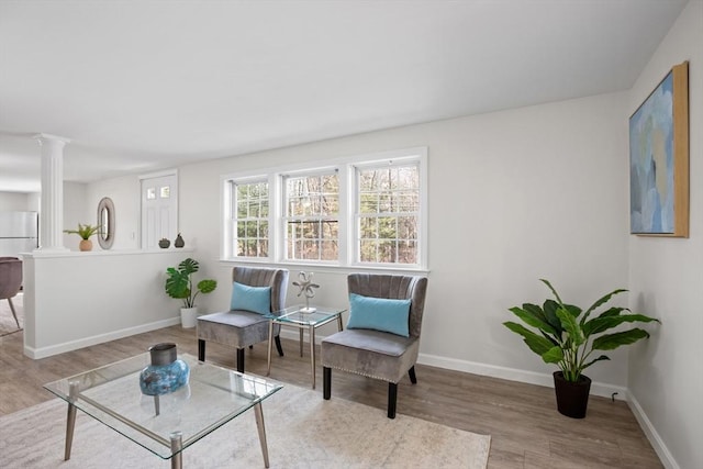 living area with decorative columns, baseboards, and wood finished floors