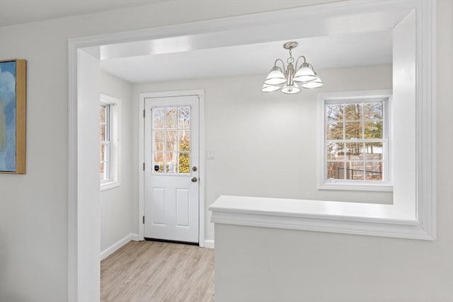 foyer entrance with light wood finished floors, a notable chandelier, a healthy amount of sunlight, and baseboards