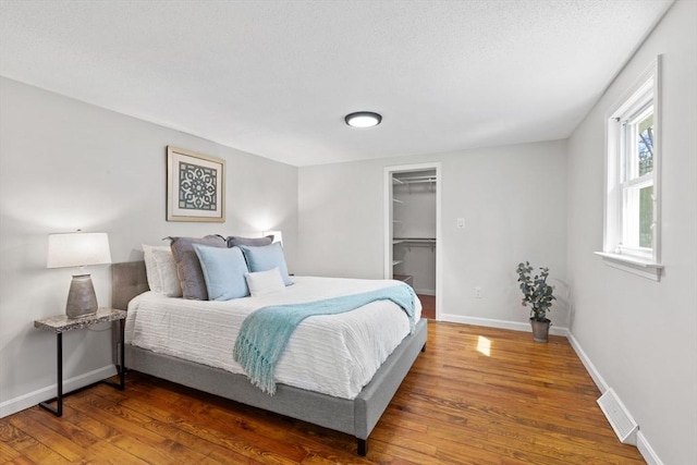 bedroom with a walk in closet, visible vents, wood finished floors, and baseboards