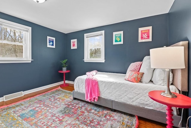 bedroom with wood finished floors, multiple windows, baseboards, and visible vents