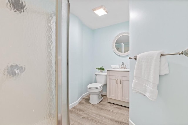 full bathroom featuring toilet, wood finished floors, baseboards, walk in shower, and vanity