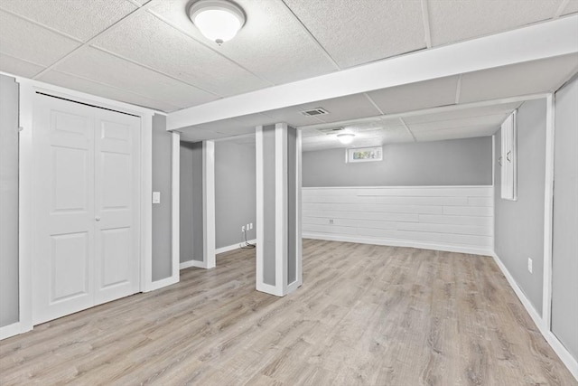 below grade area with a drop ceiling, visible vents, baseboards, and wood finished floors