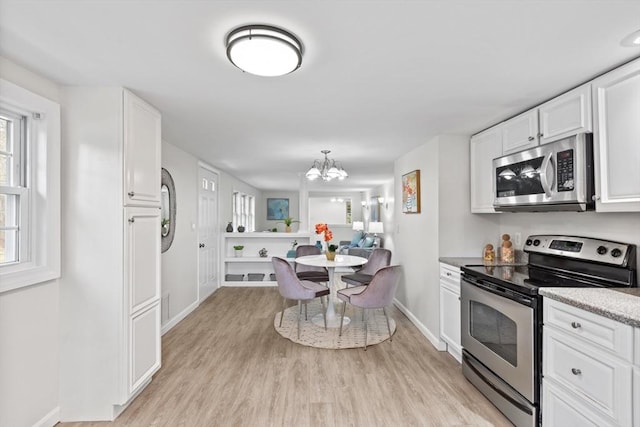 kitchen featuring baseboards, an inviting chandelier, light wood-style floors, appliances with stainless steel finishes, and white cabinetry