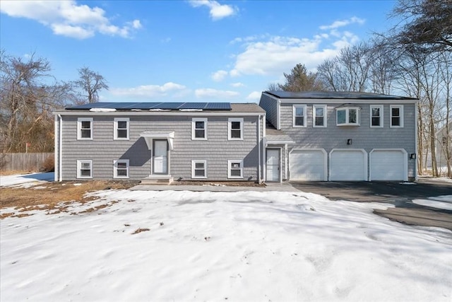 view of front of property with an attached garage, roof mounted solar panels, fence, and aphalt driveway