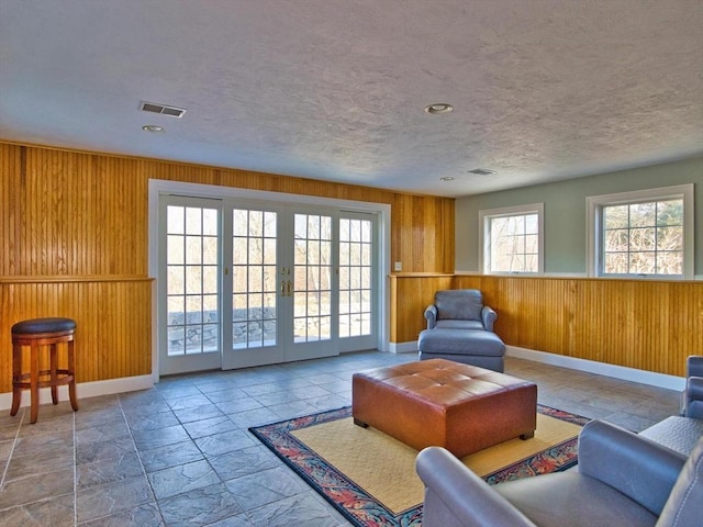 living room featuring wood walls, a textured ceiling, a wealth of natural light, and french doors