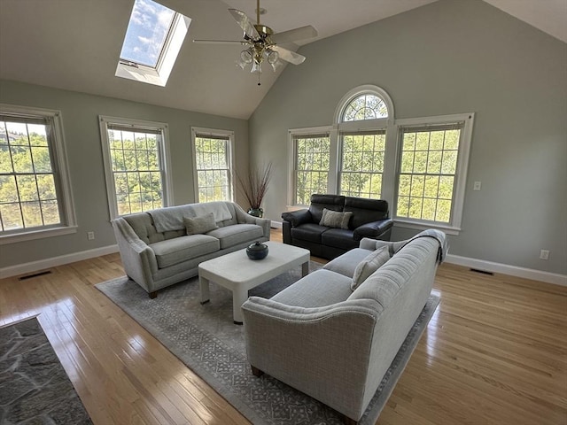 living room with ceiling fan, light hardwood / wood-style flooring, high vaulted ceiling, and a skylight