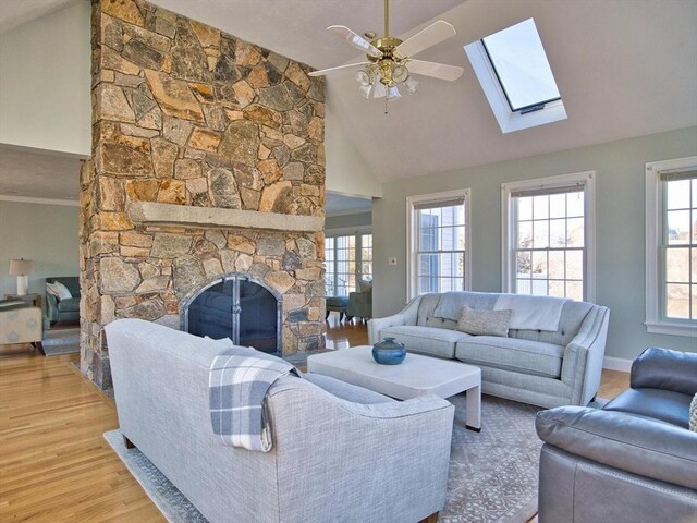 living room with vaulted ceiling, light hardwood / wood-style flooring, a stone fireplace, and ceiling fan