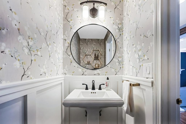 bathroom featuring a wainscoted wall, wallpapered walls, and a decorative wall