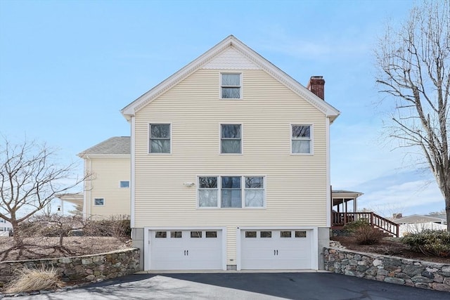 view of home's exterior with aphalt driveway, an attached garage, and a chimney