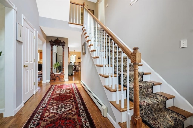 stairway with baseboards, wood finished floors, a towering ceiling, and a baseboard radiator